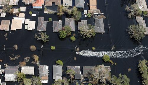 A small boat leaves a wake among houses surrounded by floodwaters.