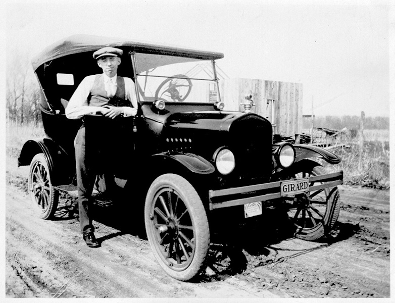 A man stands next to a Model T Ford in a black-and-white photo from the 1920s.