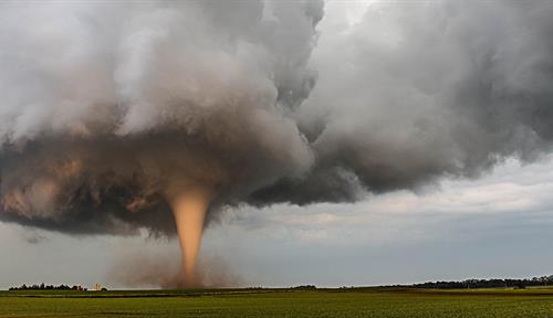 An enormous storm cloud above the plains with distinct funnel emerging from its base.